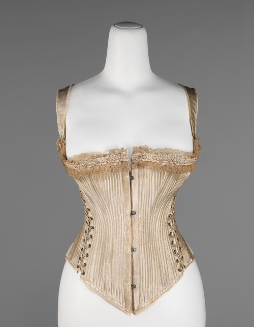 “Queen Bess” corset ca. 1876 via The Costume Institute of The Metropolitan Museum of Art “Named ‘Queen Bess’, this corset was awarded the bronze medal at the Centennial Exposition in Philadelphia in 1876 and was patented in 1877. A well documented piece, it is unique in its design, which has been carefully constructed to support the wearer’s outer garments. The straps would assist in keeping the corset in place and hinder any shifting due to the heavy fabrics, and the bustle roll at back would ease any strain the wearer might experience from the excessive weight of the skirt.”