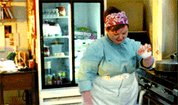 Melissa McCarthy as Sookie St James, wearing a headscarf and chef's coat, dancing in the kitchen