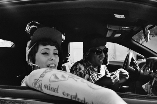 Image of Kreayshawn in the passenger seat of a car next to a black man smoking weed.