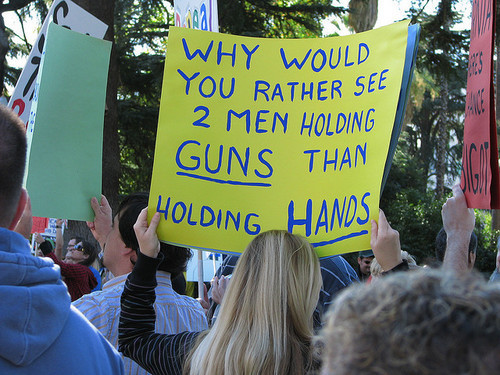 Protest banner at a gay rights march, reading: 'Why would you rather see 2 men holding guns than holding hands?'