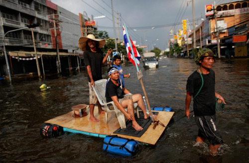 A man pulls a makeshift raft carrying his friends and with a Thai national flag attached as they make their way through a newly flooded neighborhood in Bangkok’s suburbs, on November 11, 2011 (Reuters/Damir Sagolj) via @MarcusBurtBKK