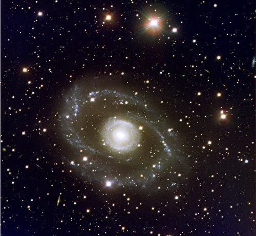 The Spectacular Spiral Galaxy ESO 269-G57 An inner &#8216;ring&#8217;, of several tightly wound spiral arms, surrounded by two outer ones that appear to split into several branches, are clearly visible. Many blue and diffuse objects are seen — most are star-forming regions. ESO 269-G57 extends over about 4 arc minutes in the sky, corresponding to nearly 200,000 light-years across. Resembling a large fleet of spaceships, many other faint, distant galaxies are visible in the background. 